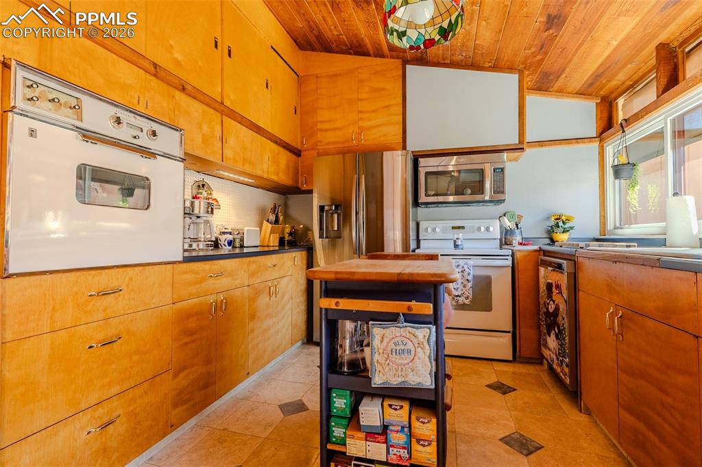 Kitchen featuring stainless steel appliances, a vaulted wood ceiling, wood finish cabinetry, light tile patterned floors, and light countertops