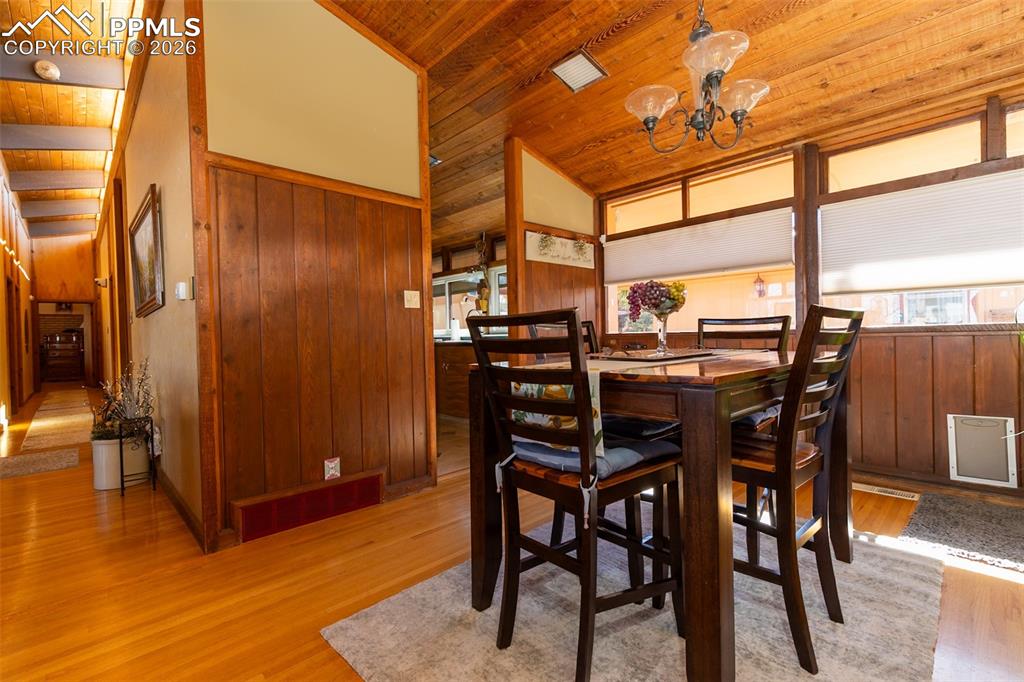 Dining space with a vaulted wooden ceiling, light wood-style flooring, wooden walls, and a chandelier