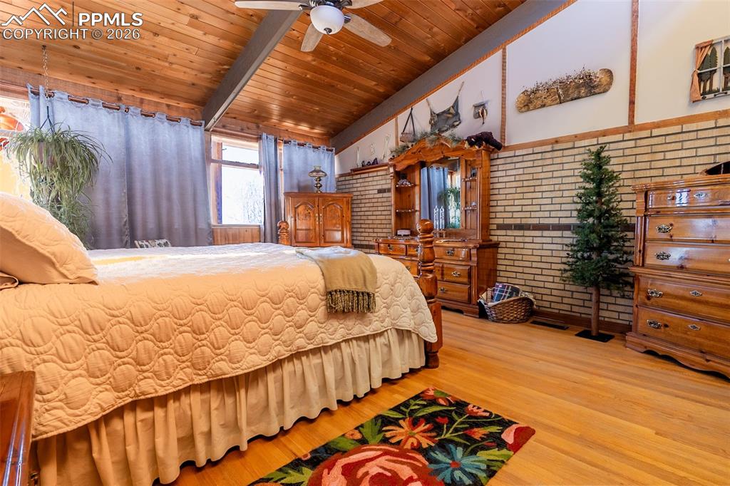 Bedroom with brick wall, light wood-style floors, wooden ceiling, a ceiling fan, and lofted ceiling with beams