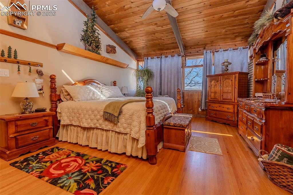 Bedroom with wooden ceiling, a ceiling fan, light wood finished floors, and vaulted ceiling with beams