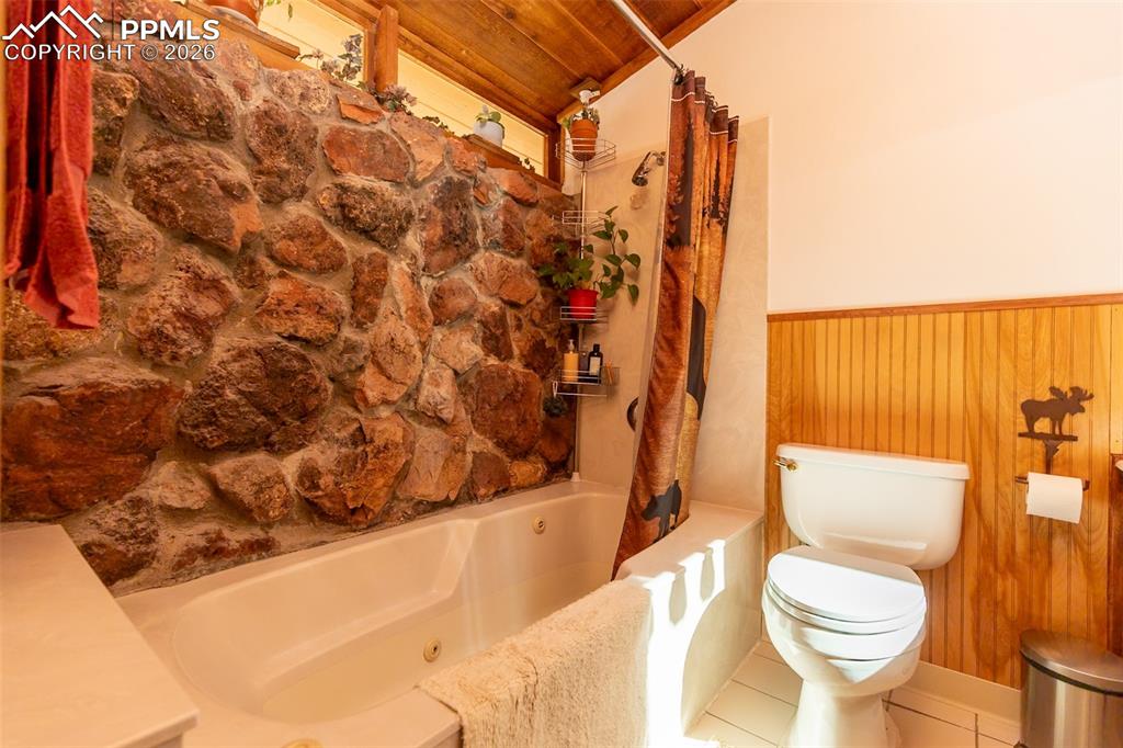 Full bathroom with wooden walls, wood ceiling, a wainscoted wall, tile patterned floors, and a combined bath / shower with jetted tub