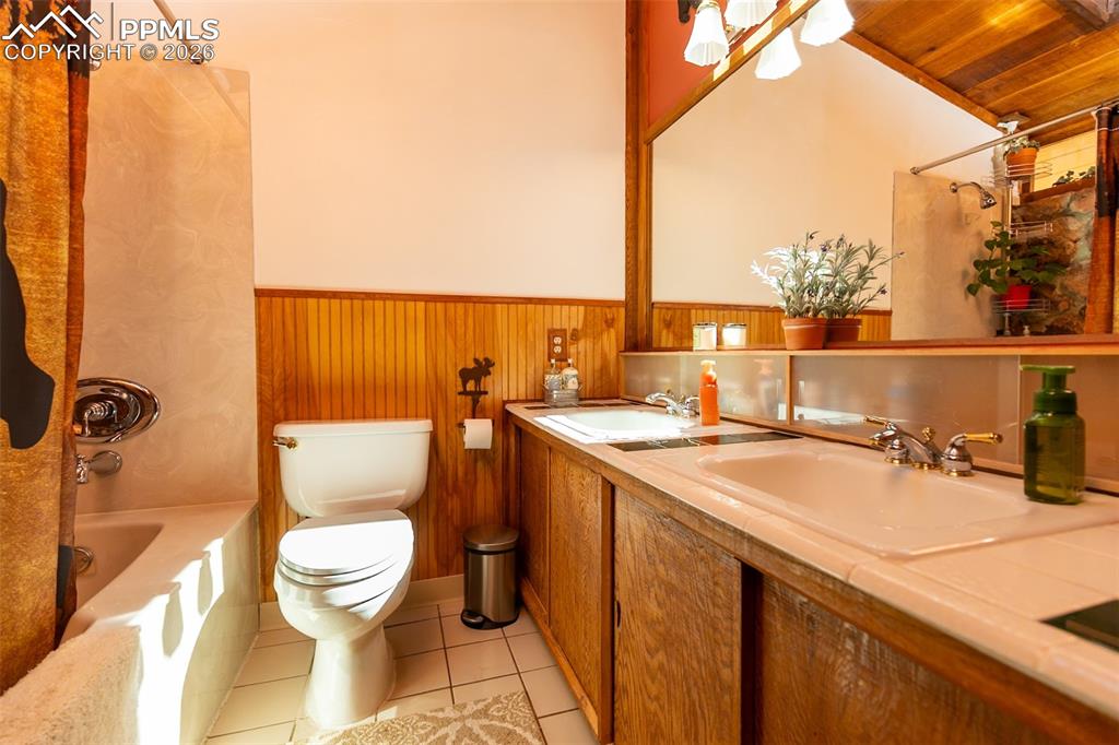 Full bath with wainscoting, double vanity, wood walls, shower / bath combo, and light tile patterned floors