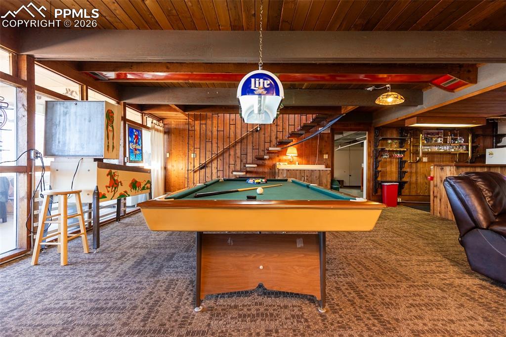 Recreation room with wooden walls, a wooden ceiling with exposed beams, pool table, and a community bar