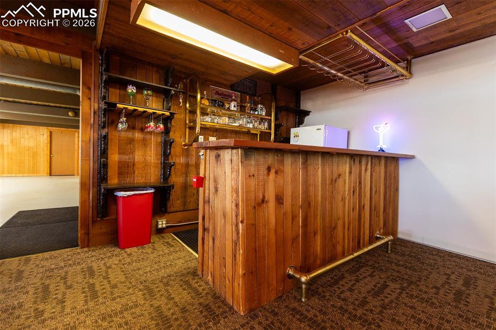 Indoor dry bar with wooden ceiling, dark carpet, white fridge, and wood walls