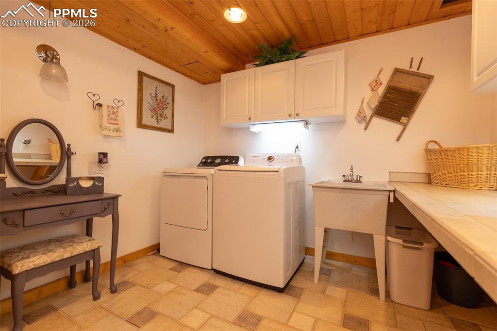 Laundry area featuring wood ceiling, cabinet space, separate washer and dryer, and light stone finish floors