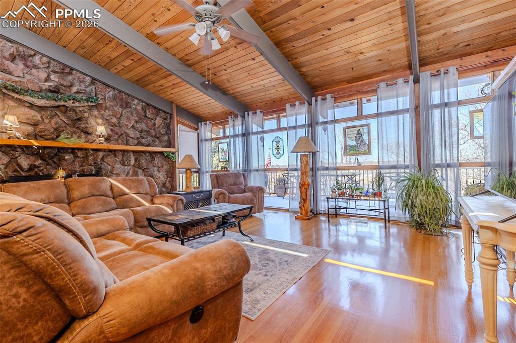 Living area with a high wooden beamed ceiling, a ceiling fan, wood finished floors, and floor to ceiling windows