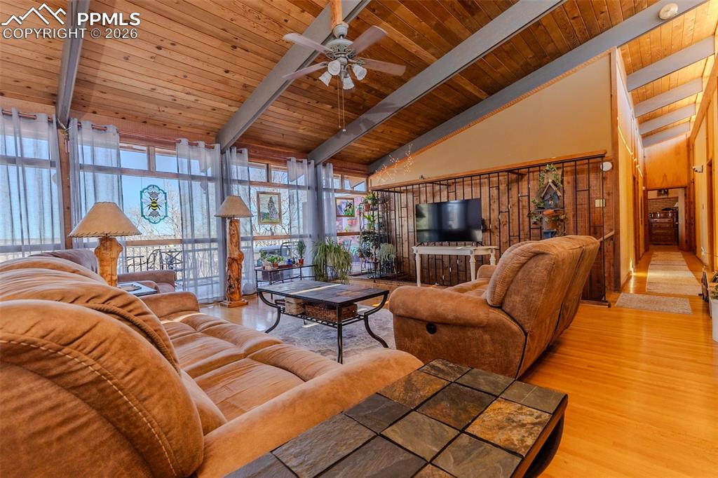 Living area featuring a ceiling fan, wood finished floors, and a high wood beamed ceiling