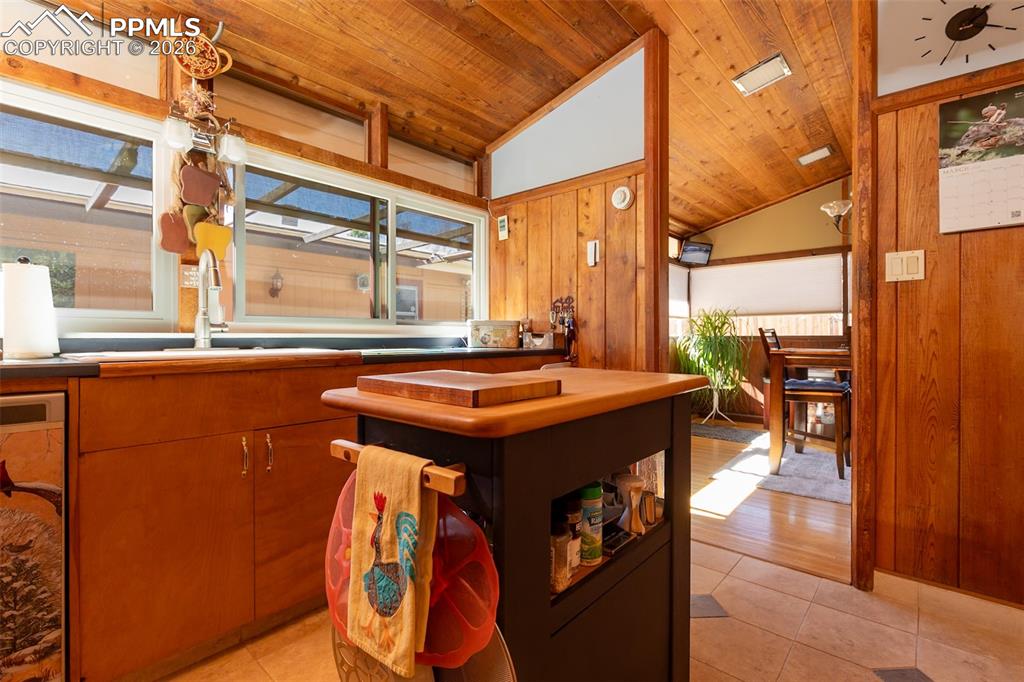 Kitchen with a vaulted wood ceiling, light tile patterned flooring, wood finish cabinetry, stainless steel dishwasher, and wood walls