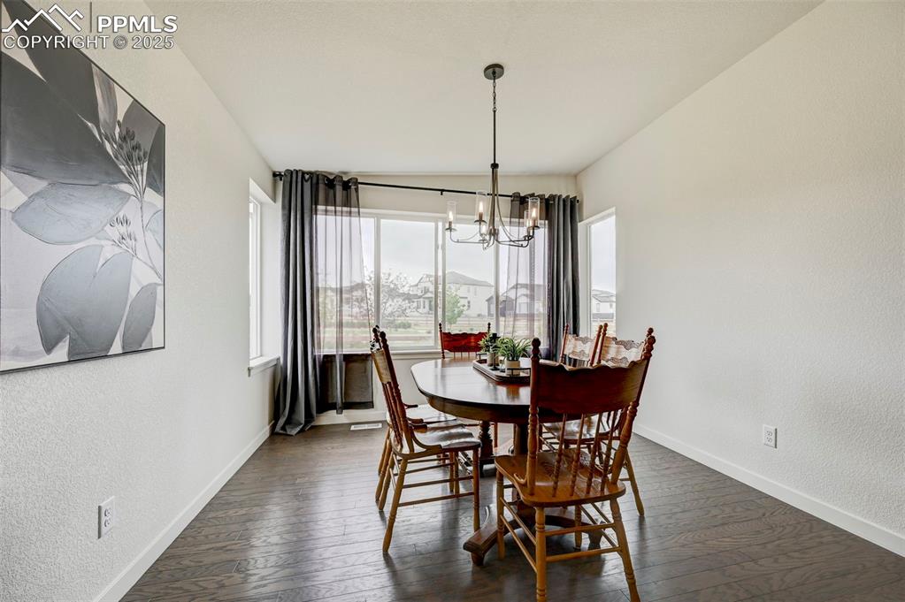 Dining room with a chandelier, baseboards, dark wood-type flooring, and a textured wall