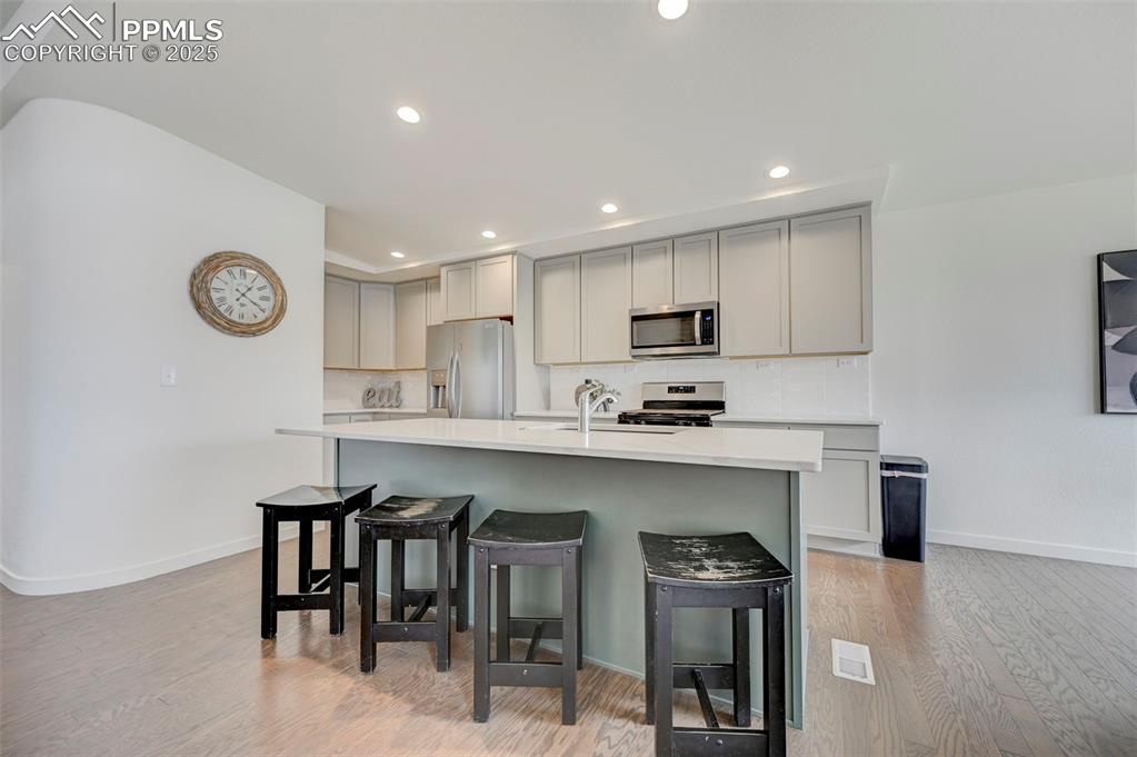 Kitchen featuring stainless steel appliances, gray cabinetry, light wood-style floors, a kitchen breakfast bar, and recessed lighting