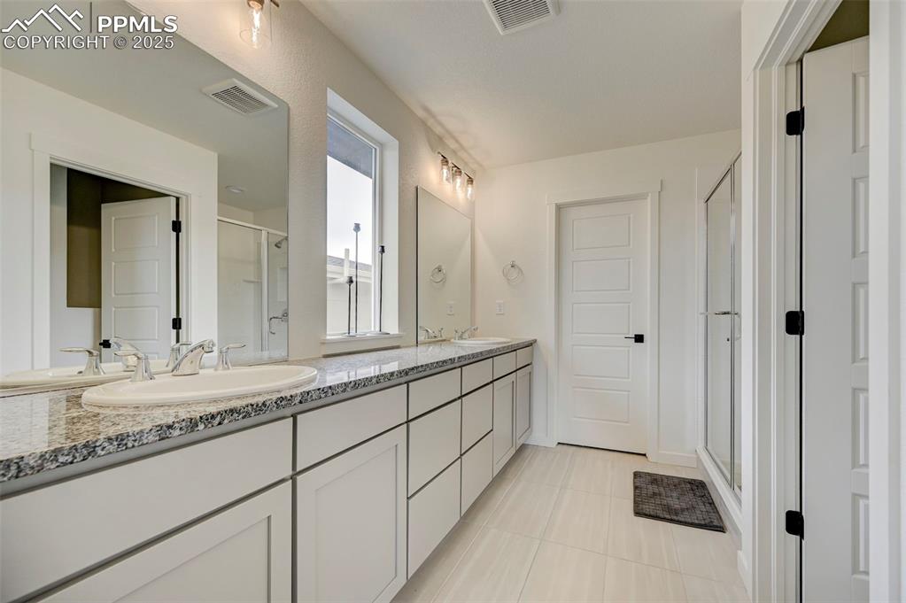 Full bath featuring a shower stall, double vanity, and tile patterned floors