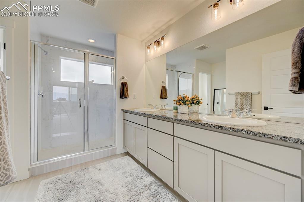 Bathroom featuring double vanity, a shower stall, and wood finished floors