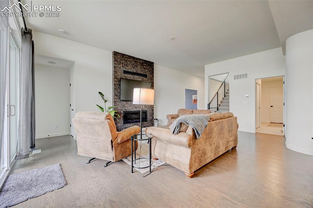 Living room with light wood finished floors, stairway, a stone fireplace, and baseboards