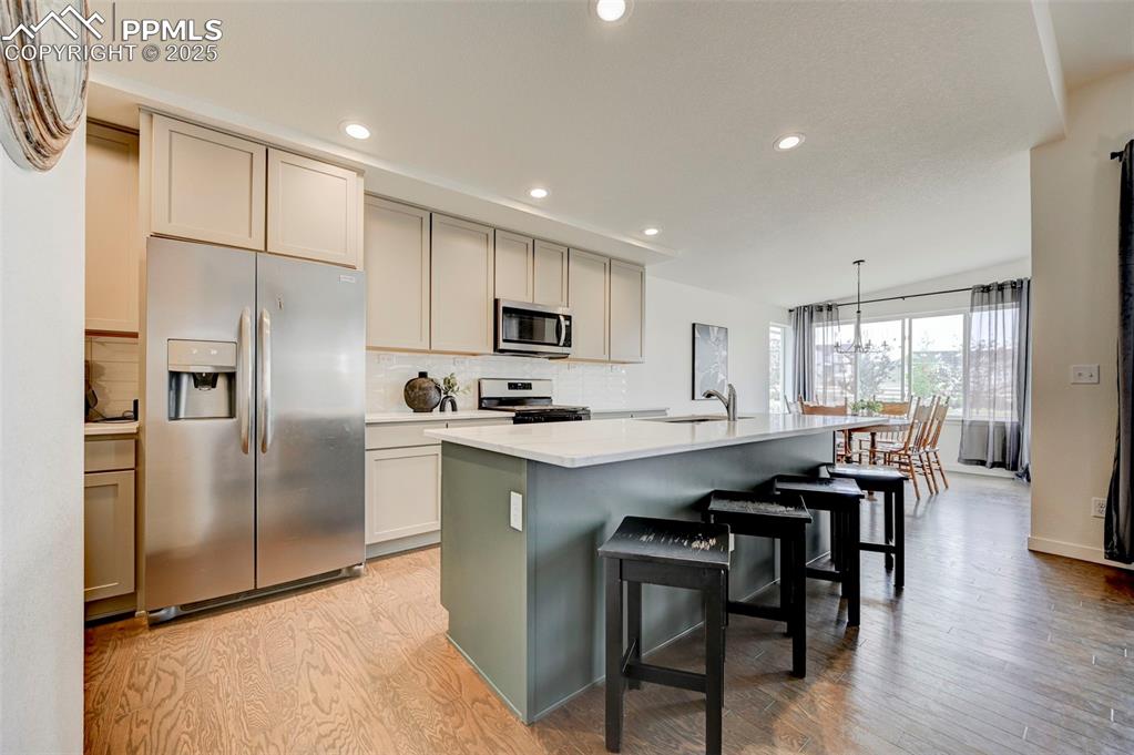 Kitchen featuring stainless steel appliances, a sink, backsplash, recessed lighting, and a center island with sink