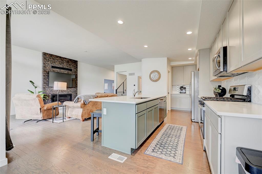 Kitchen with stainless steel appliances, a sink, light wood-type flooring, open floor plan, and gray cabinetry