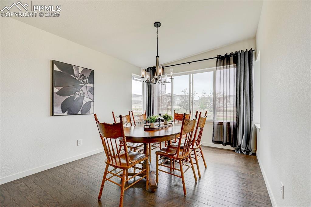 Dining space with a chandelier, baseboards, dark wood-style floors, and a textured wall