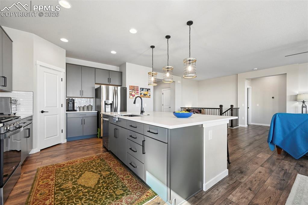 Kitchen with gray cabinetry, dark wood finished floors, stainless steel appliances, and tasteful backsplash