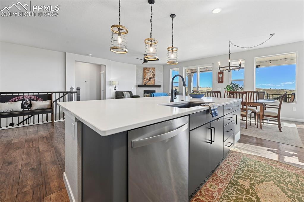 Kitchen featuring dishwasher, dark wood-style floors, an island with sink, suspended lighting, and a fireplace