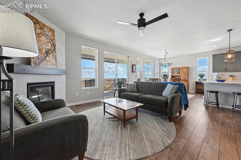 Living area with a tiled fireplace, dark wood-style floors, a ceiling fan, hanging lights, and a textured ceiling