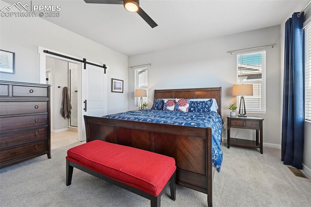 Primary Bedroom featuring a barn door, light carpet, ceiling fan, and multiple windows