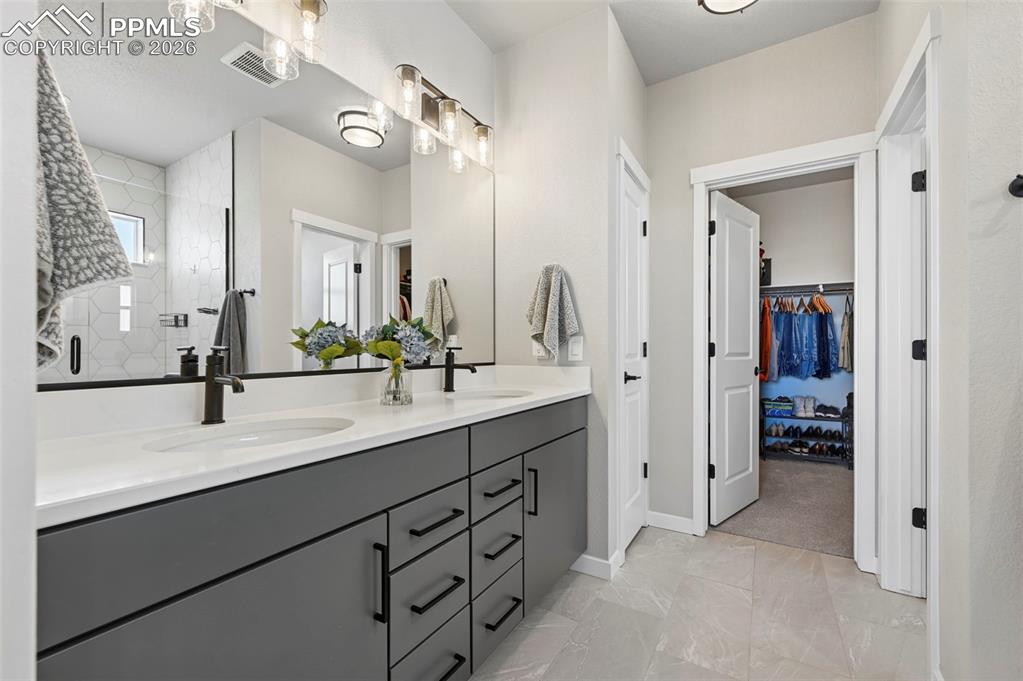 Primary bath featuring double vanity, a quartz finish shower, and a walk in closet