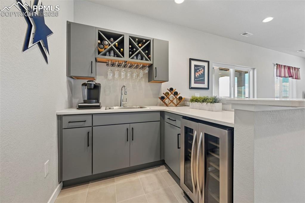 Indoor wet bar featuring gray cabinets, wine cooler, light countertops, a textured wall, and recessed lighting