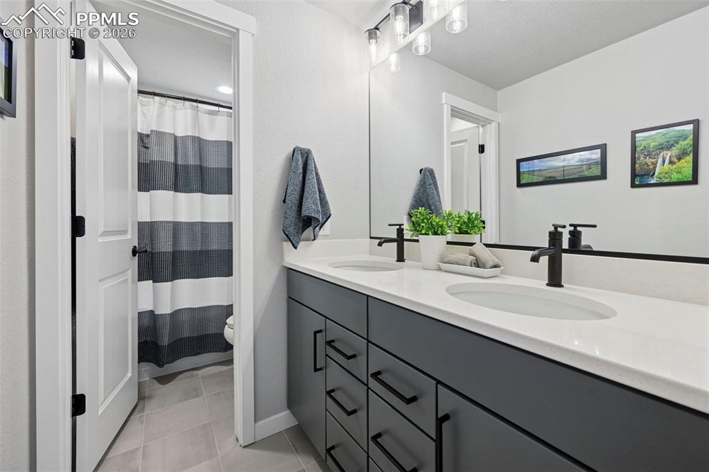 Basement Full bathroom with double vanity, curtained shower, and light tile patterned floors