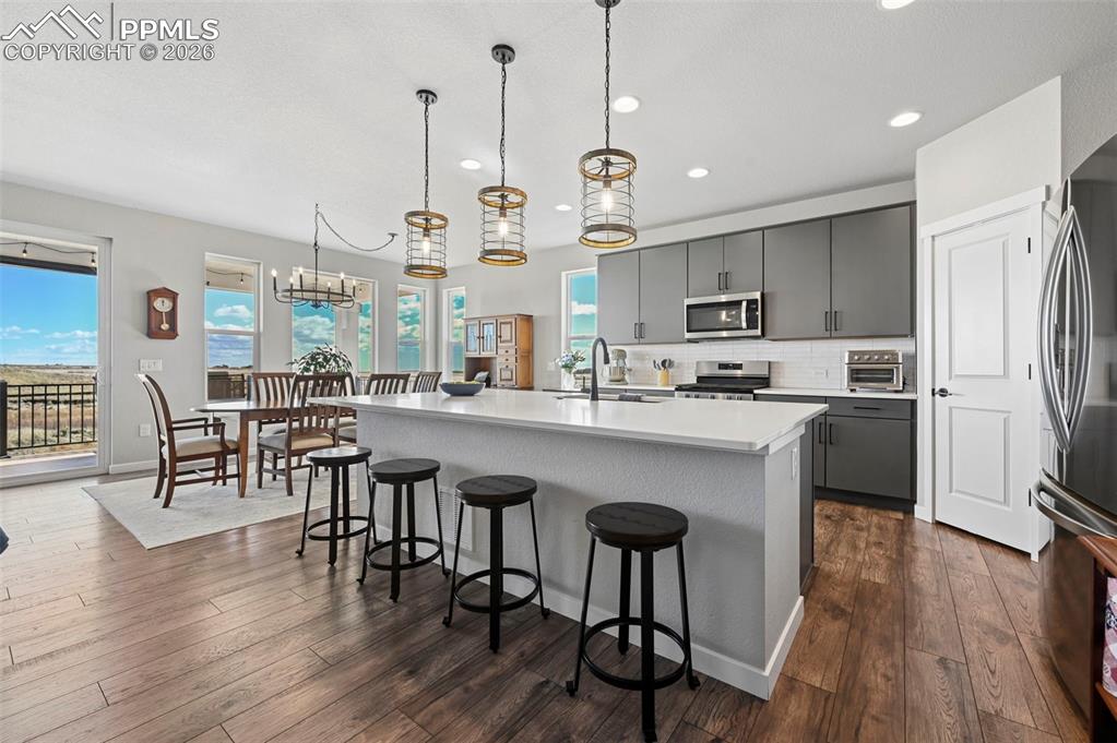 Kitchen featuring gray cabinetry, a kitchen island with sink, a breakfast bar area, backsplash, and stainless steel appliances