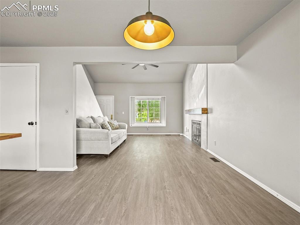 Living room featuring a ceiling fan, baseboards, wood finished floors, and a large fireplace
