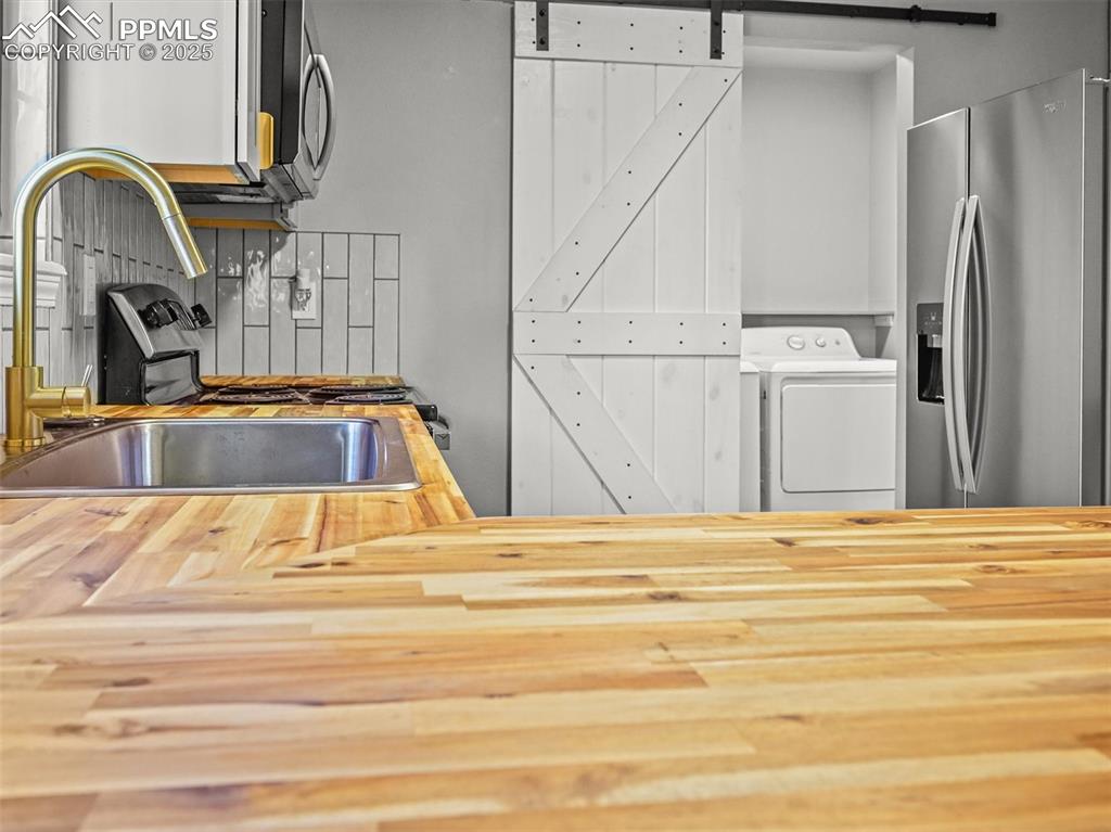 Kitchen featuring wood counters, appliances with stainless steel finishes, a sink, and a barn door