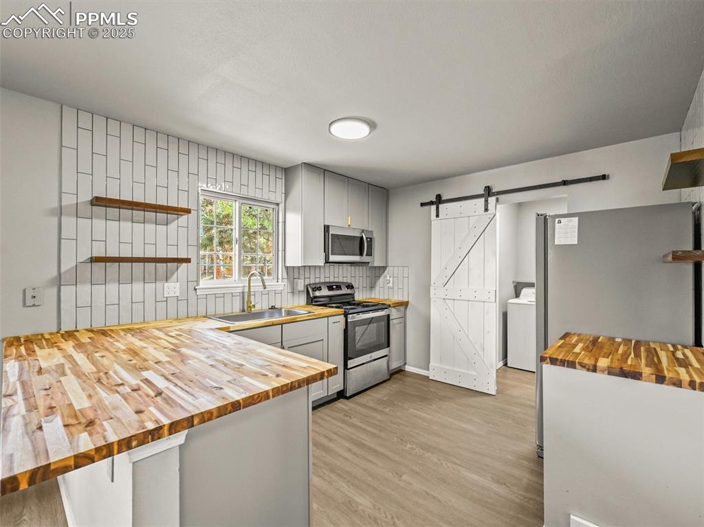 Kitchen featuring butcher block countertops, appliances with stainless steel finishes, a barn door, and open shelves