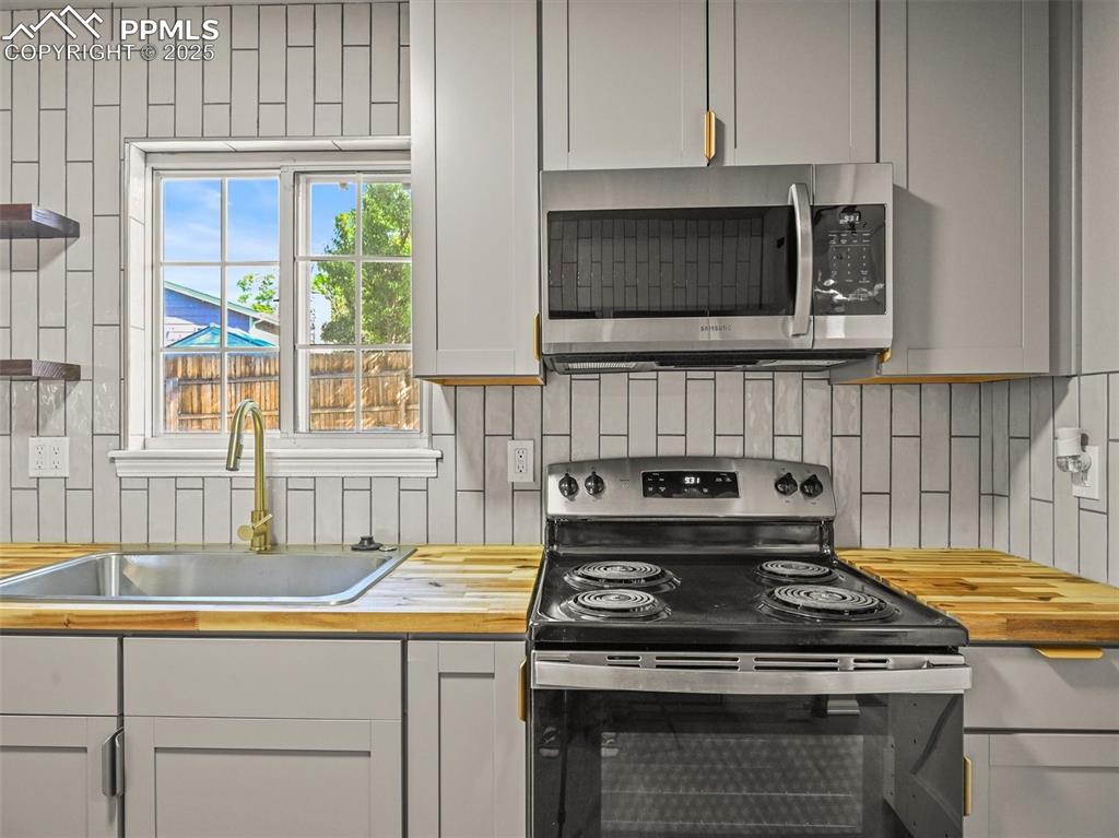 Kitchen with stainless steel appliances, wooden counters, a sink, and decorative backsplash