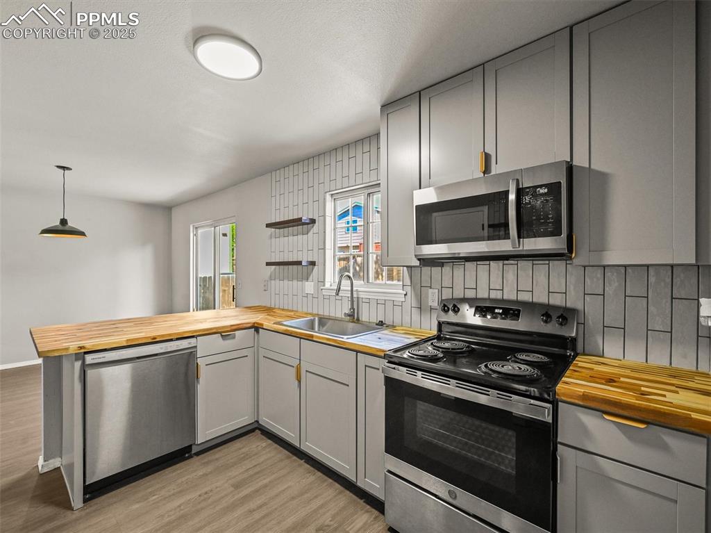 Kitchen with butcher block countertops, stainless steel appliances, a sink, gray cabinets, and backsplash