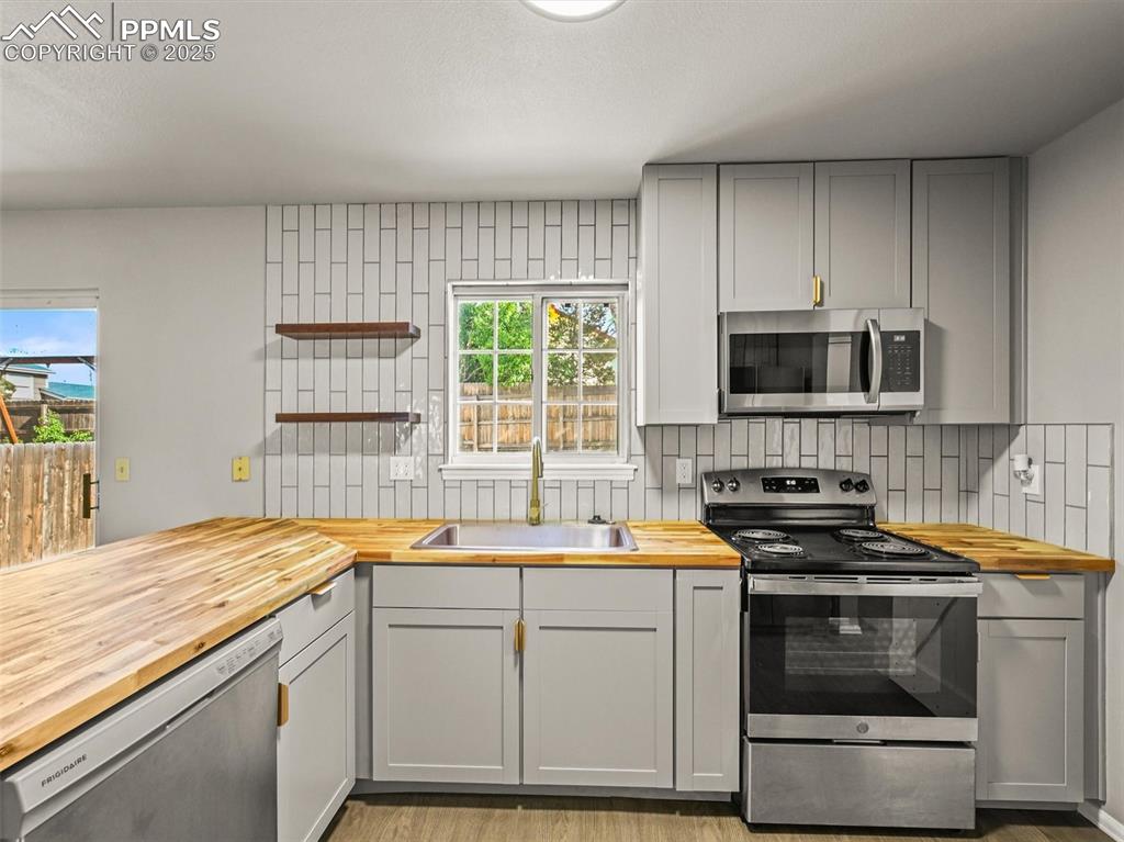 Kitchen featuring butcher block countertops, appliances with stainless steel finishes, a sink, and tasteful backsplash