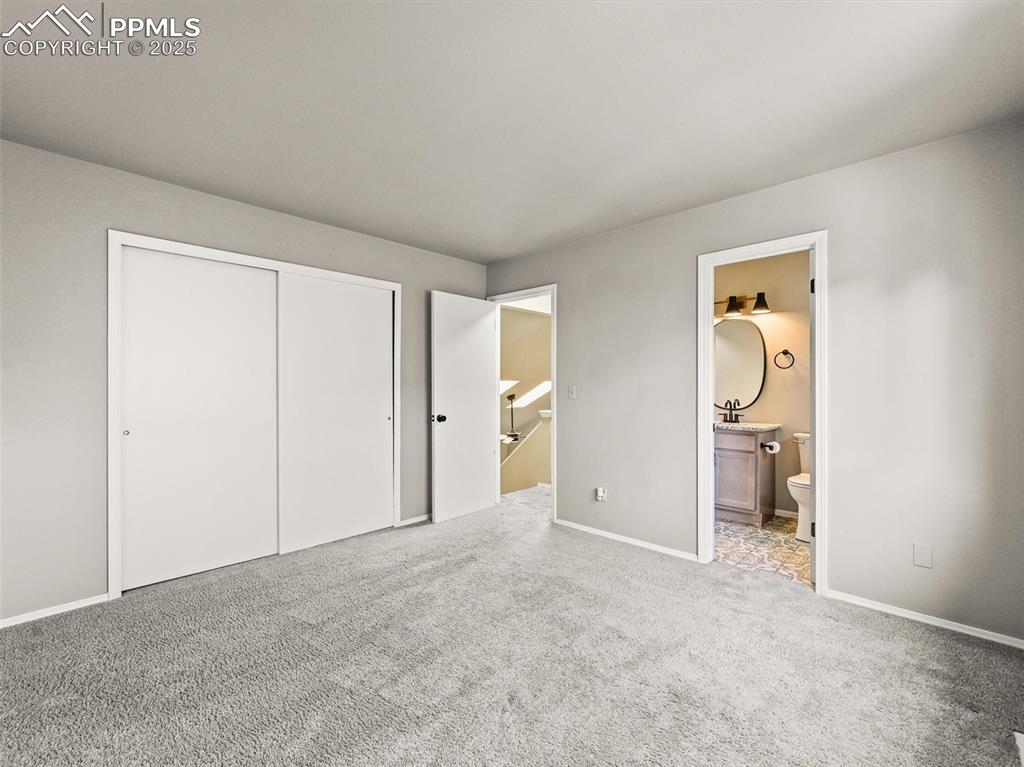 Unfurnished bedroom featuring carpet flooring, a closet, ensuite bathroom, baseboards, and a sink