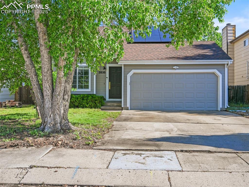 View of front of property with concrete driveway, roof with shingles, an attached garage, and solar panels