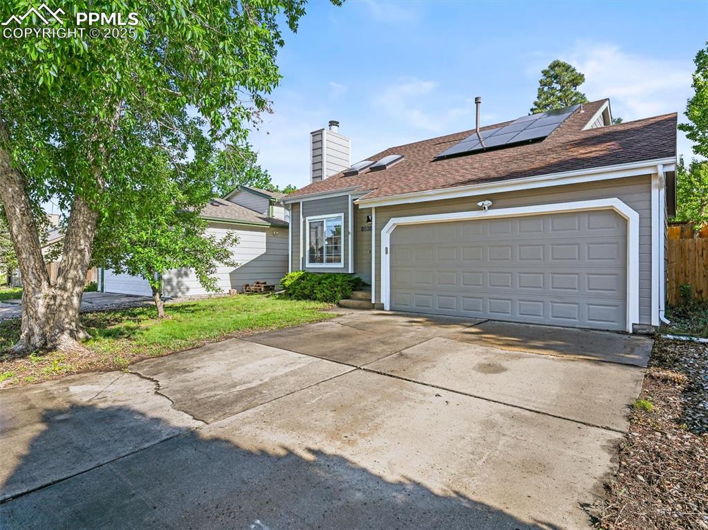 View of front of house featuring concrete driveway, solar panels, a chimney, an attached garage, and roof with shingles