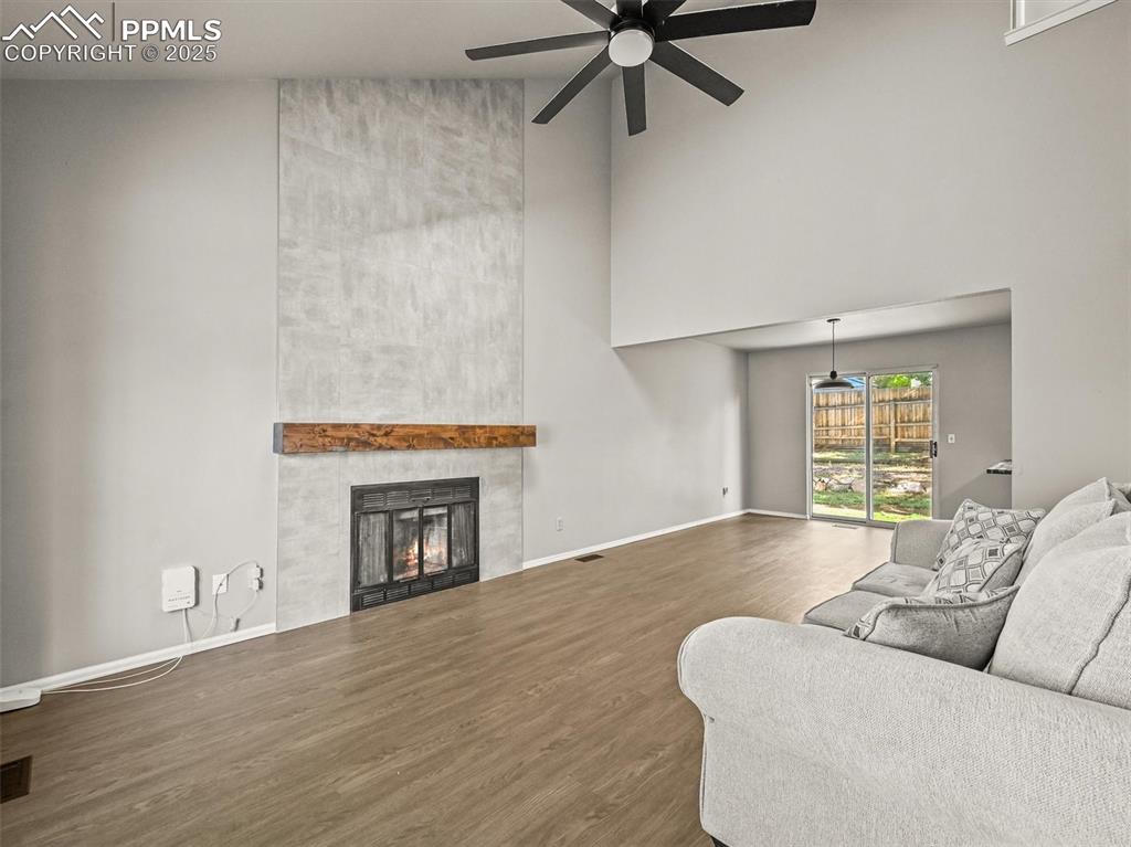 Living room with a towering ceiling, a ceiling fan, wood finished floors, a tile fireplace, and baseboards