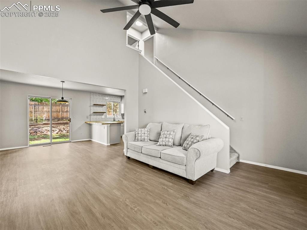 Living area featuring stairs, a ceiling fan, wood finished floors, baseboards, and high vaulted ceiling