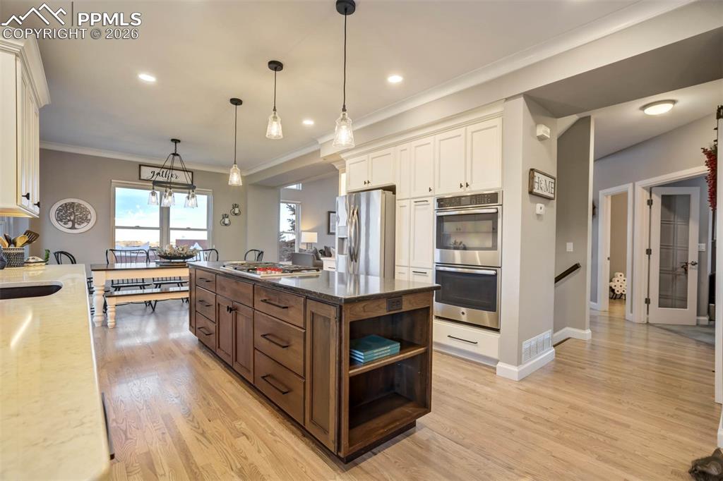 Custom Kitchen featuring one of two large islands with granite/stone countertop and Wolf 5 burner stainless steel gas cook top and featuring extra storage and shelving, stainless steel appliances, custom molding,pendant, recessed lighting and hardwood floors.