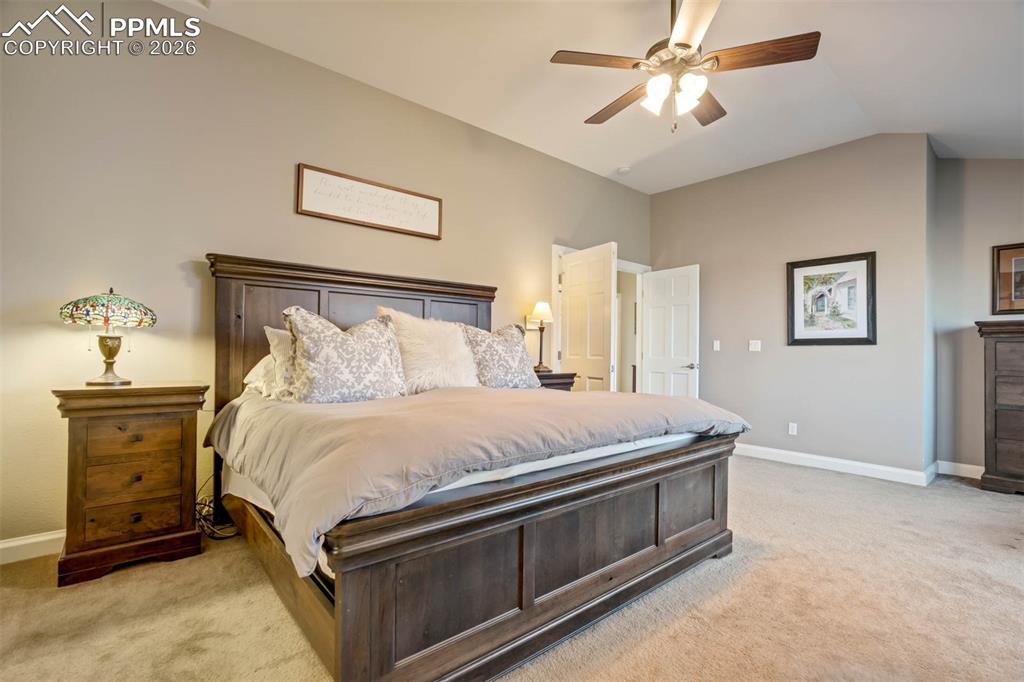 Spacious primary bedroom featuring light carpet, lofted ceiling and ceiling fan w/lights.