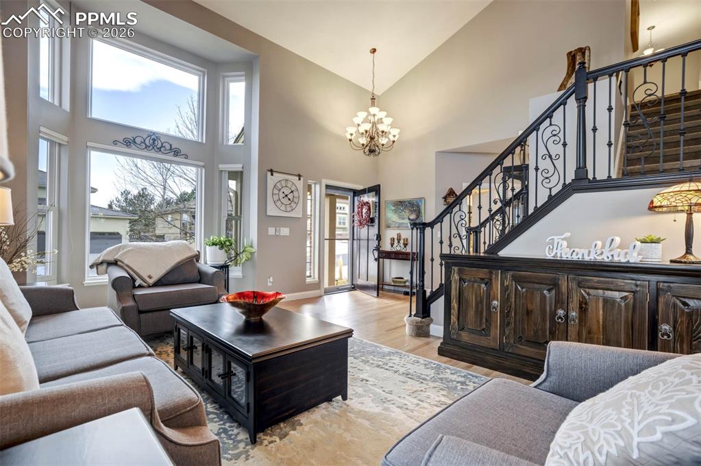 Enter into the Living area featuring high vaulted ceiling, stairway with wrought iron bannisters, beautiful hardwood flooring, newer windows and a large chandelier