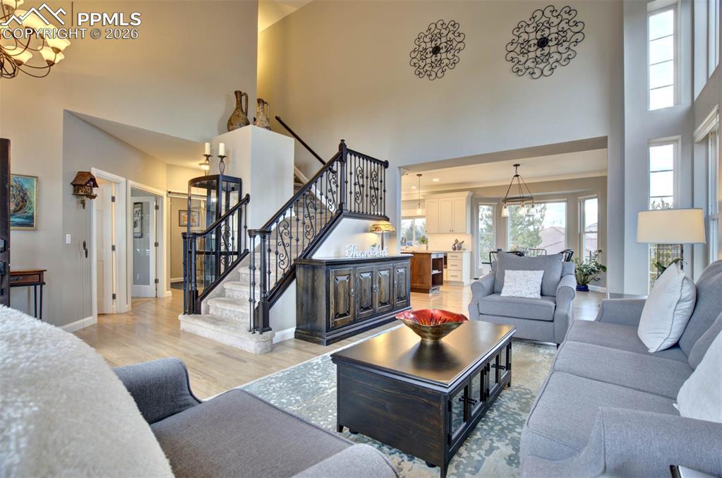 Living area with a chandelier, staircase with wrought iron bannisters and a niche for artwork, hardwood floors, and a towering ceiling