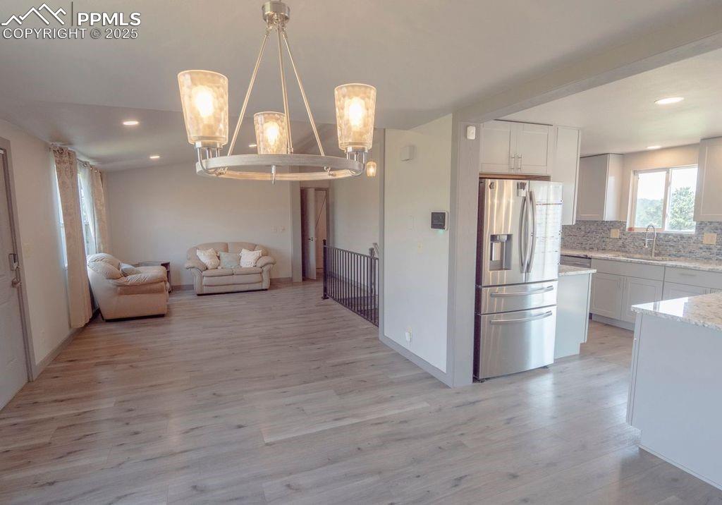 Kitchen featuring open floor plan, stainless steel refrigerator with ice dispenser, light wood-style flooring, backsplash, and recessed lighting