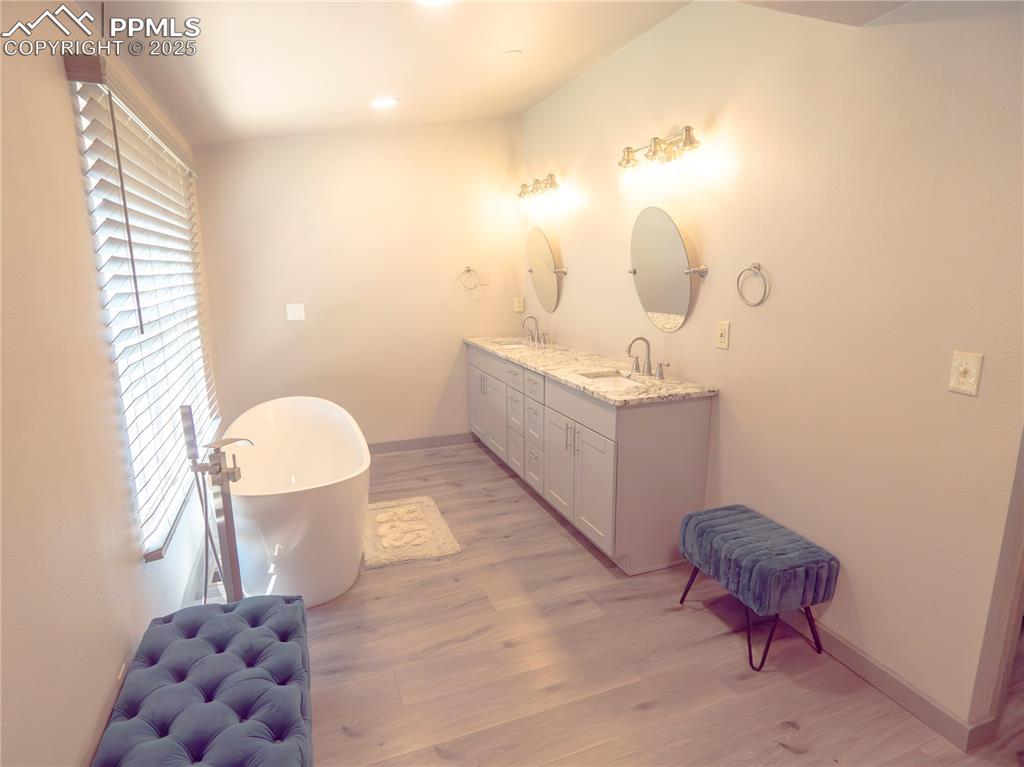 Full bathroom featuring double vanity, a freestanding bath, wood finished floors, and recessed lighting