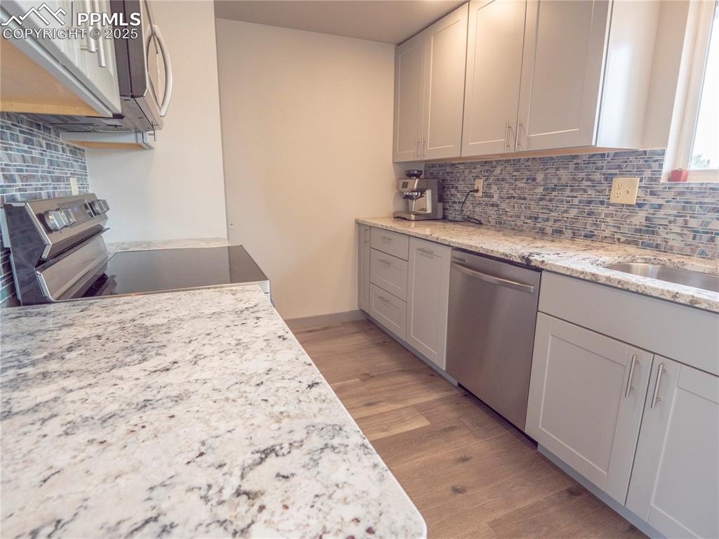 Kitchen featuring backsplash, appliances with stainless steel finishes, light wood-style floors, and light stone countertops
