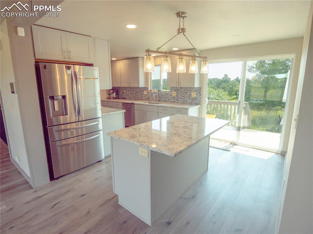 Kitchen featuring appliances with stainless steel finishes, light wood-type flooring, decorative backsplash, light stone counters, and recessed lighting