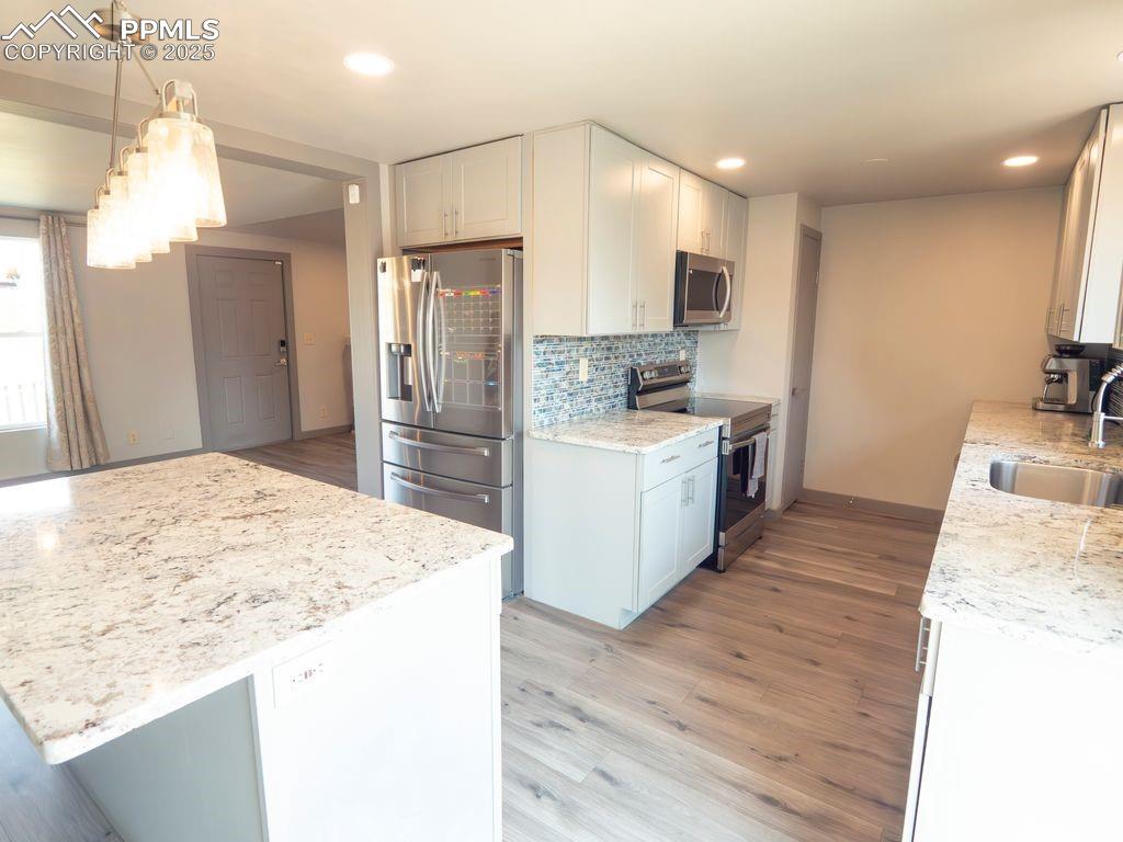 Kitchen featuring light wood-style floors, appliances with stainless steel finishes, backsplash, light stone countertops, and white cabinets