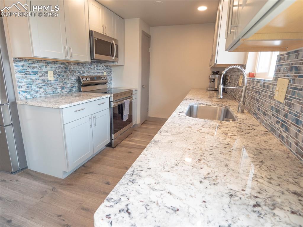 Kitchen featuring backsplash, appliances with stainless steel finishes, light wood-style flooring, light stone counters, and recessed lighting