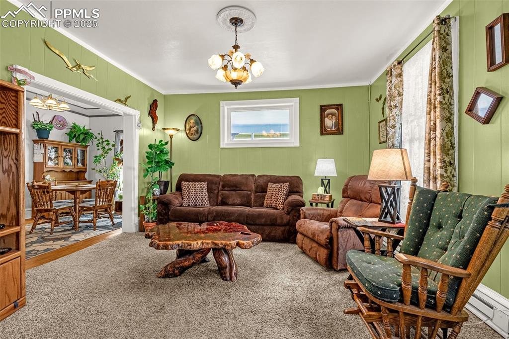 Carpeted living area with a chandelier, baseboard heating, and crown molding